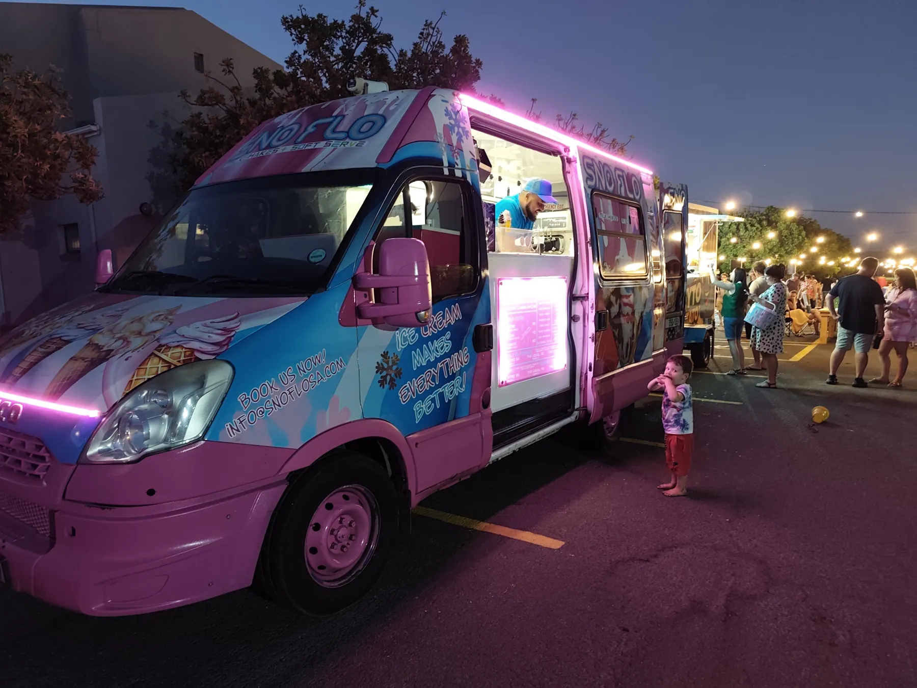 The SNO FLO ice cream bus lit up in pink at a night market